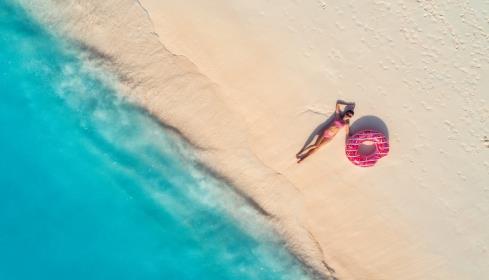 摄图网_300877307_鸟瞰美丽的轻躺着的女人,粉红色的甜甜圈游泳环白色的沙滩上,靠近大海,日落时波浪暑假苗条女孩的最高视野,清澈的蔚蓝的（企业商用）.jpg